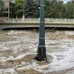 Rain-swollen Boulder Creek flowed around a marker that shows historic flood levels on Friday in Boulder, Colo.