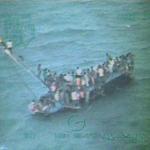 About 100 Haitians sat on the hull of a sail freighter after it grounded and capsized near Staniel Cay, Bahamas.