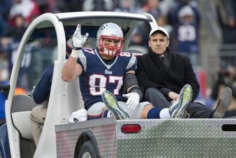 Rob Gronkowski, riding with Dr. Thomas Gill, waves as he’s carted off the field after injuring his knee. He was taken to the hospital Sunday and was expected to have an MRI Monday.
