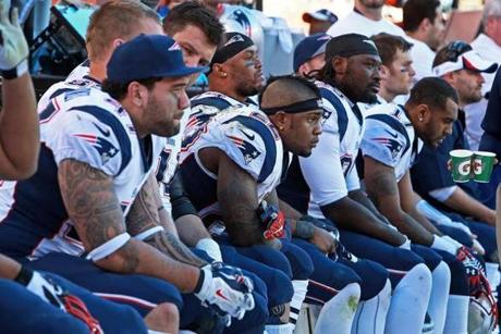 Michael Hoomanawanui (left) and Stevan Ridley (22) can only watch as the faces on the Patriots’ bench tell the story with time winding down on the their season in Denver.
