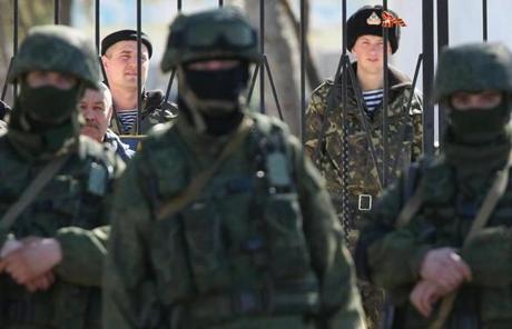 Ukrainian soldiers stood inside the gate of a Ukrainian military base as unidentified heavily-armed soldiers stood outside the gates.
