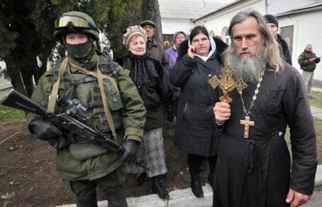 An Orthodox priest held a crucifix next to one of many armed men in military fatigues blocking access to the Ukrainian border.
