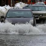 Vehicles drove through a flooded Portland Street in Cambridge Saturdayafter a water main ruptured.