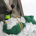 A crew removed snow by the bagful from a flat portion of the roof  at South Shore Plaza in Braintree early last month. 