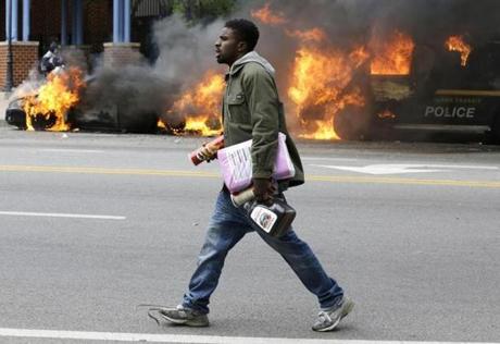 A man carried items from a store as police vehicles burned after the funeral of Freddie Gray in Baltimore. 
