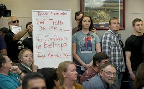 Bob Welch (standing, at left) and Jim Dillon held a sign at a public hearing about the Jade Helm 15 military training exercise in Bastrop, Texas, last April.
