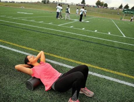 John D. O'Bryant High School junior Lila Hernandez foam rolled her back as she and the track team worked out during the opening of the West Roxbury Education Complex Raiders Field on Saturday.
