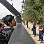 Migrants looked through a fence between Serbia and Hungary, near Horgos, Serbia, on Tuesday. Hungary has declared a state of emergency in two of its southern counties because of the migration crisis, giving special powers to police and other authorities. 