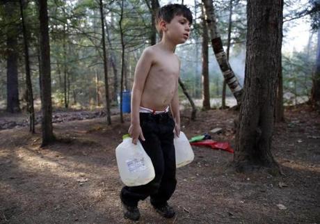 Oxford, Maine -- 5/4/2015-- Strider carried gallon jugs of water over to Lanette after filling them from a spigot behind the camper so that she could wash dishes and heat some of it on the small stove inside to bathe the boys with a washcloth. Jessica Rinaldi/Globe Staff Topic: 31strider Reporter: Sarah Schweitzer
