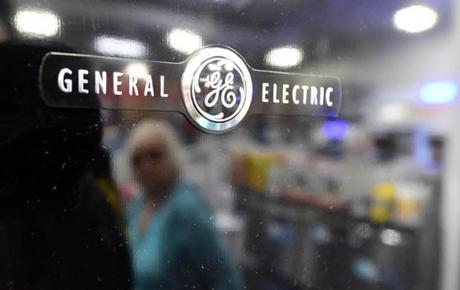 A woman is reflected on the black door of a General Electric refrigerator. 
