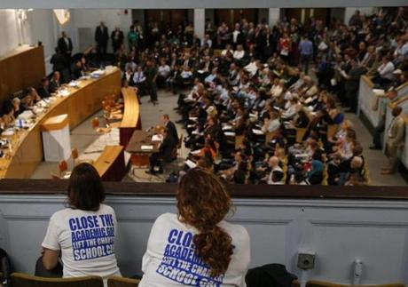 Women wearing t-shirts that read, ?Close the academic gap. Lift the Charter School cap.? lean over a balcony at the State House Thursday.

