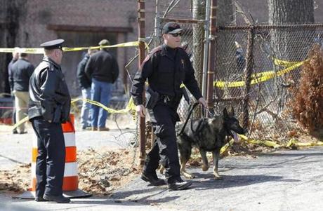 A Rhode Island State Trooper escorts a dog as they exits a dig behind a mill complex at the intersection of Branch Ave. and Woodward Rd., in Providence, R.I., looking for human remains Wednesday, March 30, 2016. (Photo/Stew Milne for the Boston Globe)

