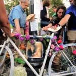 Mourners reach out to touch a ghost bike at a vigil for Amanda Phillips, who was killed while riding a bike in Inman Square.