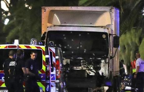 Police officers stand near a van, with its windshield riddled with bullets, that plowed into a crowd in Nice.
