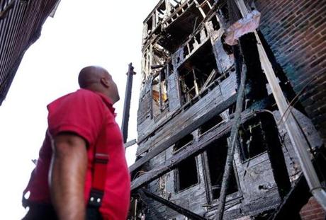 Charlestown-07/22/2016-Boston firefighters remained at the scene of a 6-alarm apartment fire on Bunker Hill Street in Charlestown that caused extensive damage to the multi-apartment building. A firefighter looks for hot spots at the rear of the building. Boston Globe staff photo by John Tlumacki(metro)
