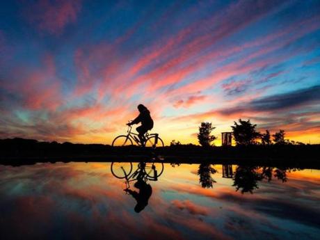 A bicyclist is reflected at sunset in a large puddle in the parking lot of Scusset Beach in Sandwich. 
