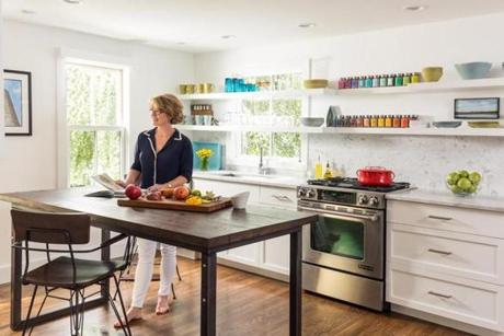  Homeowner Pamela Shepard cuts vegetables at the island, where she and her husband also eat quick meals. The Elston stools are from Crate & Barrel. Colorful spice jars by Victoria Gourmet fit perfectly on a 4-inch-deep portion of shelving above the range. The couple keep mostly clear glasses in front of the window so sunlight and the view shine through.
