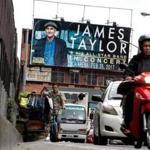 A clothing vendor pedaled his bicycle past a billboard promoting a planned concert by US singer James Taylor in Manila. 