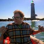 Dave Waller navigates a small dinghy past rocks surrounding the lighthouse he and his wife bought at auction in 2013.