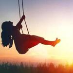 Happy laughing child girl on swing in sunset summer