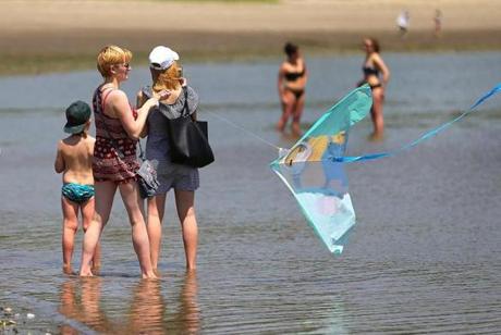 South Boston-05/17/2017- A woman flys a kite as she an others venture ankle-deep into the water of Carson Beach. City beaches will open Thursday just in time for a scroching spring day predicted to be in the 90's. JohnTlumacki/ The BostonGlobe (metro)
