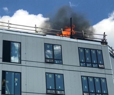 The fire in a Dorchester condo building last month started when an improperly installed exhaust pipe, visible in front of the flames in this photo, ignited wood framing in the upper level of the Treadmark building.

