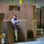Abbott-Action has a state of the art corrugated box making facility. A worker checks the label on one of the stacks of precut boxes that are ready to be shipped out. The boxes lie flat in the stacks and are folded into boxes by the clients.