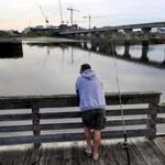 Somerville-8/12/17- A man fishes from a pier on the Mystic River behind Assembly Row near where the contruction on the new Wynn Casio takes place across the water in Everett. The Amelia Earhart Dam is to the left and the MBTA bridge spans the river to the right. A new pedestrian and bike bridge is proposed somewhere to cross the river close to this location. John Tlumacki/Globe Staff(metro)
