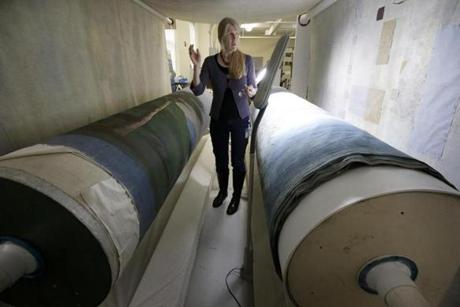 Photo textile conservator Kate Tarleton stands between two oversized spools holding a portion of the 1848 