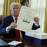 President Donald Trump shows off the tax bill after signing it in the Oval Office of the White House, Friday, Dec. 22, 2017, in Washington.