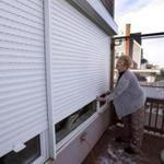 Marshfield resident Glenda Adams lowered protective metal storm curtains over the seaside facing her sunroom in preparation for Thursday's storm and high tides.