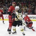 Boston Bruins' Brad Marchand (63) chases the puck with Carolina Hurricanes' Jaccob Slavin (74) as Hurricanes goalie Cam Ward keeps an eye on the puck during the first period of an NHL hockey game in Raleigh, N.C., Tuesday, March 13, 2018. (AP Photo/Gerry Broome)