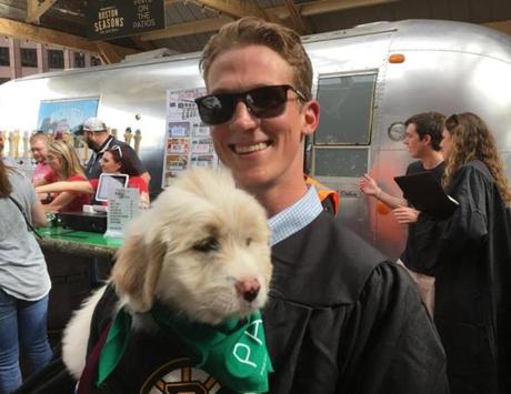 Northeastern graduate Jake Heney holds a puppy at the opening ceremonies for The Patios on Boston City Hall Plaza.
