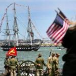 People stood on Castle Island with flags as the USS Constitution was saluted by the Concord Independent Battery (rear) and the 101st Field Artillery that fired in a return salute. 