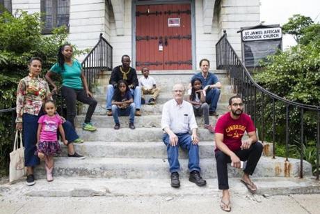 Boston, MA - 6/14/2018 - (left to right) Neighborhood resident Tai Pai-Yung Jimenez, her daughter Coco, Kristen Willis,Haviv Saccoh, Sidi Saccoh Sira Saccoh, John Jon Ellertson, Carmel Schafer, Mark Schafer, and Johnathan Correia sit on the steps of the St. James African Orthodox Church in Boston, MA, June 14, 2018. They and other local residents are seeking to have the building preserved as a Boston landmark, which would serve as a defense against a real estate firm plans to demolish the building and build condos on the property. ( (Keith Bedford/Globe Staff)
