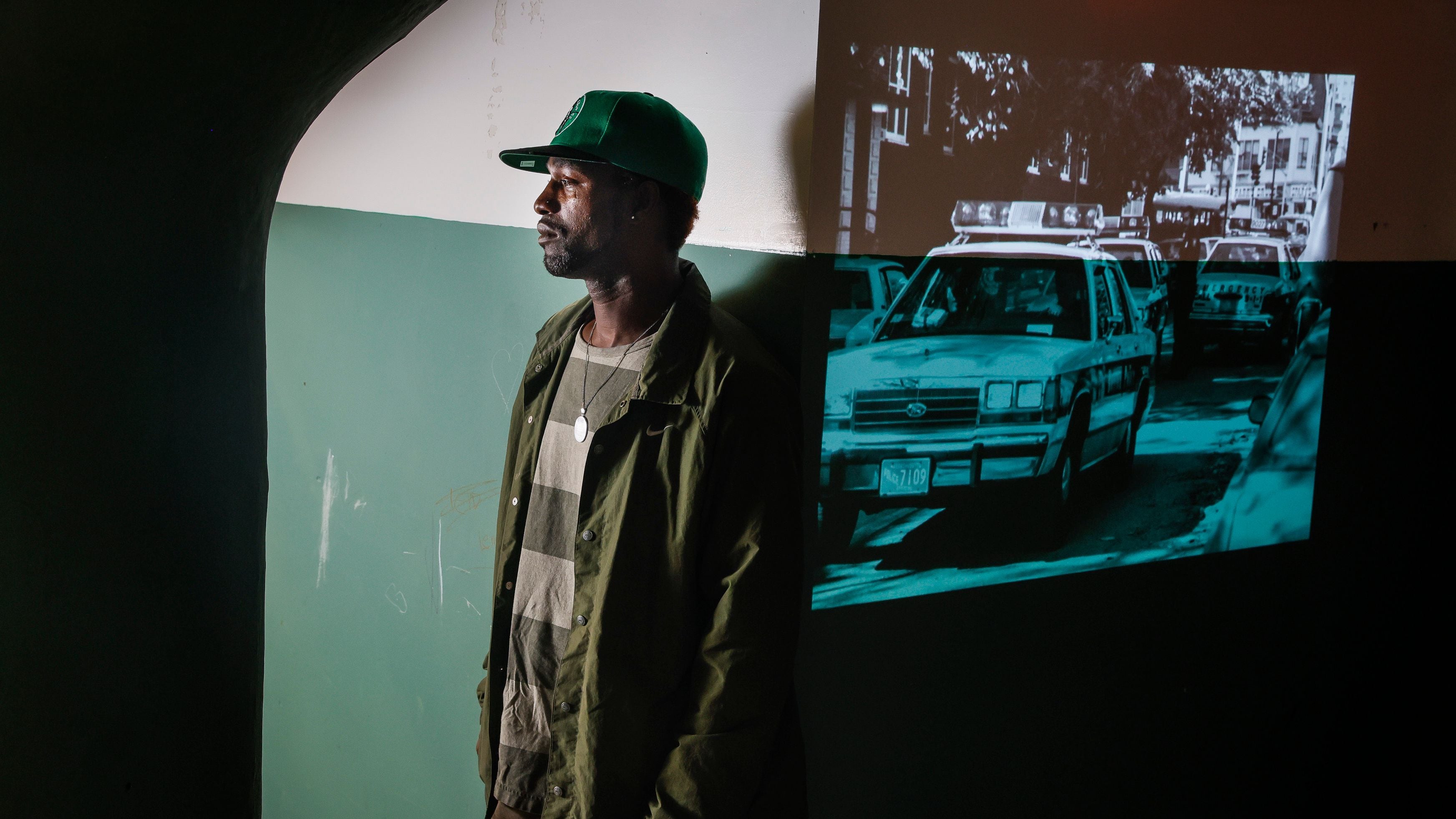 DonJuan Moses poses for a portrait next to a projection of police cars in Mission Hill 