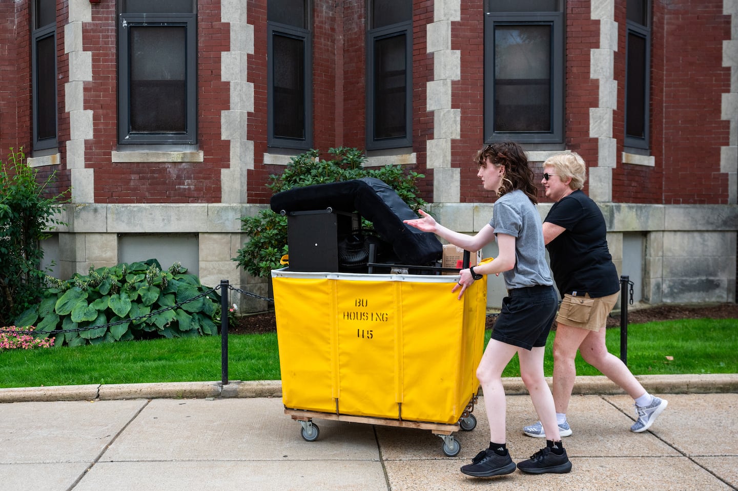 Boston University sophomore Ailsa Smith (left) and Karin Smith push a yellow cart containing housing items while moving into Alisa’s campus housing, which is overseen by resident assistants.