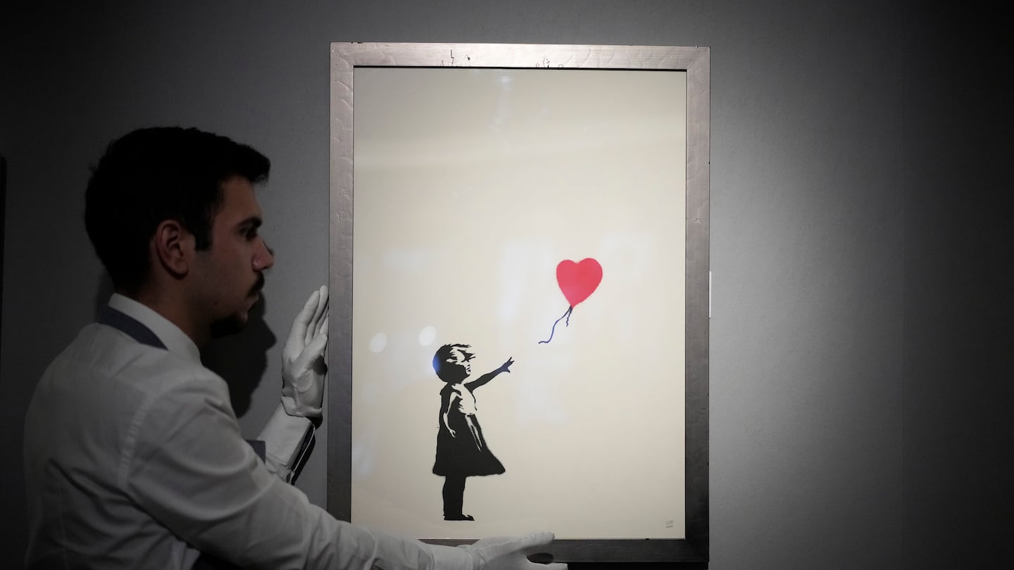 A staff member with a print of "Girl with Balloon, 2004" by British street artist Banksy, at Bonhams auction house in London, Nov. 8, 2021.