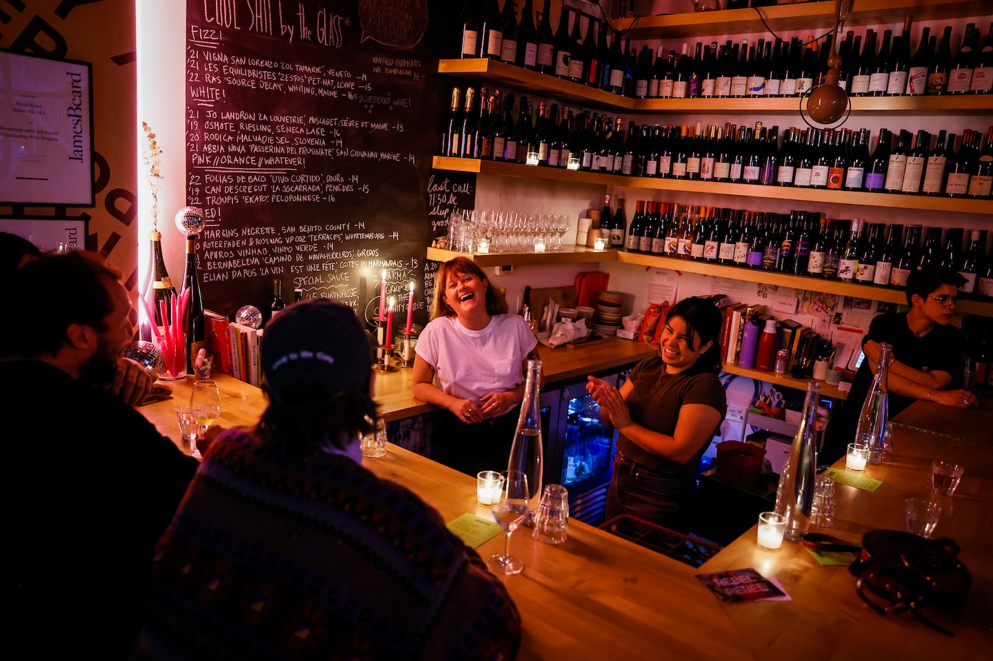 Lauren Friel (left) owner of Rebel Rebel, chatted with customers while working at her wine bar in Bow Market in Somerville. The restrictive Boston liquor license system has pushed throngs of innovative chefs to neighborhood towns with laxer laws, including Brookline, Somerville, and Cambridge.