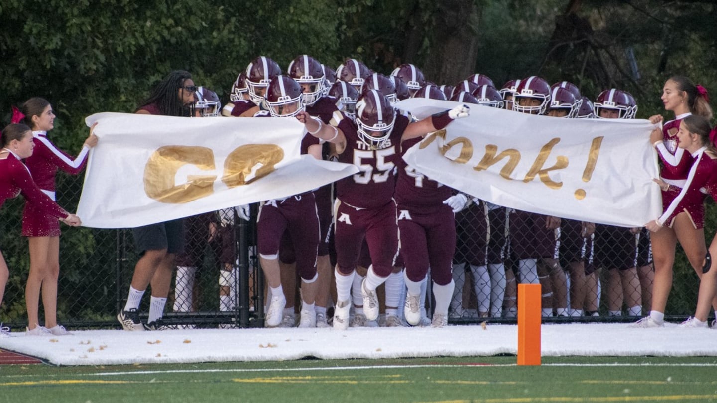 Senior captain Dom Frallicciardi (55) runs through a banner held up by the Algonquin Regional cheerleaders that reads "Go Gonk" on Sept. 13, 2024. Despite the strong opening, Algonquin lost to visiting Doherty Memorial High School, 31-14.