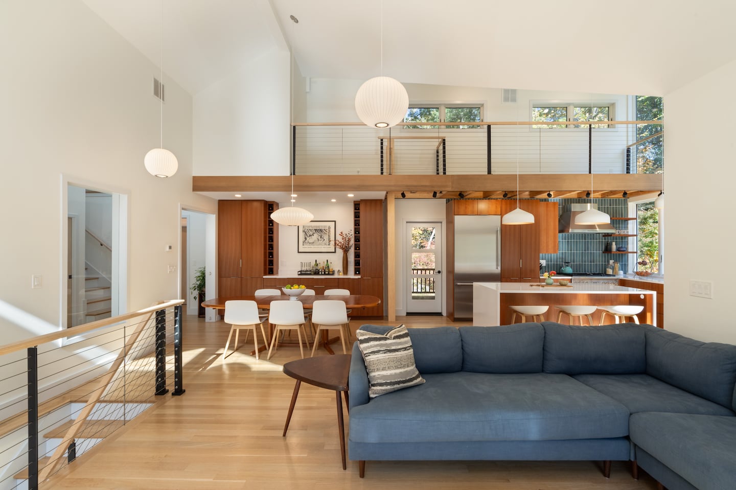 A loft, inspired by a family lake house, runs above the dining area and kitchen, with a vertical ladder and a door to the porch between them.