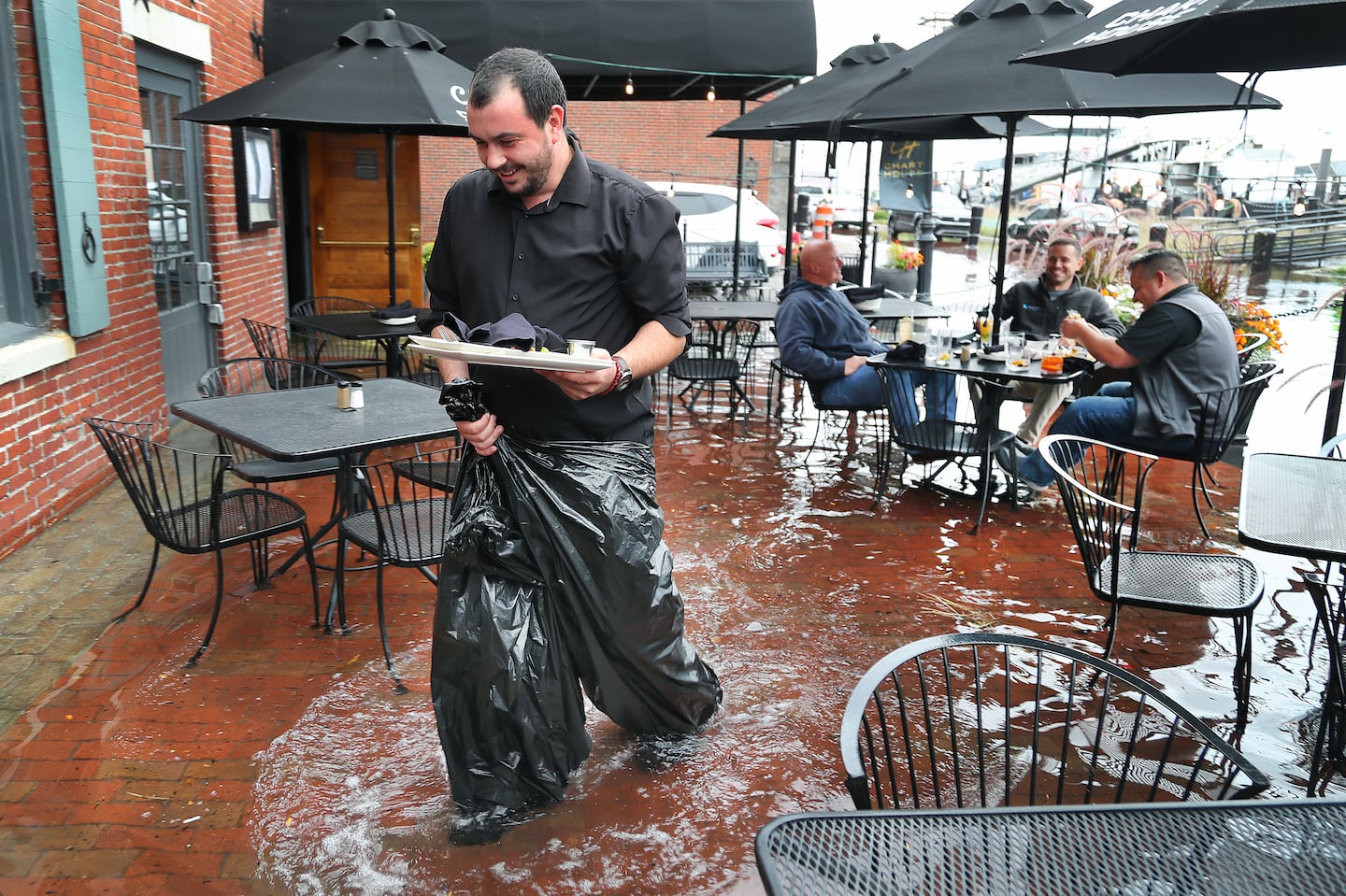 The high tide flooded sections of Long Wharf in Boston at its height just after 1 p.m. Joe Hebert, Greg Prall, and Rick Paoni had lunch on the outside patio of the Chart House on Long Wharf despite over a foot of water flooding the patio. Waiter Milan Grbovic used trash bags to keep dry while working.