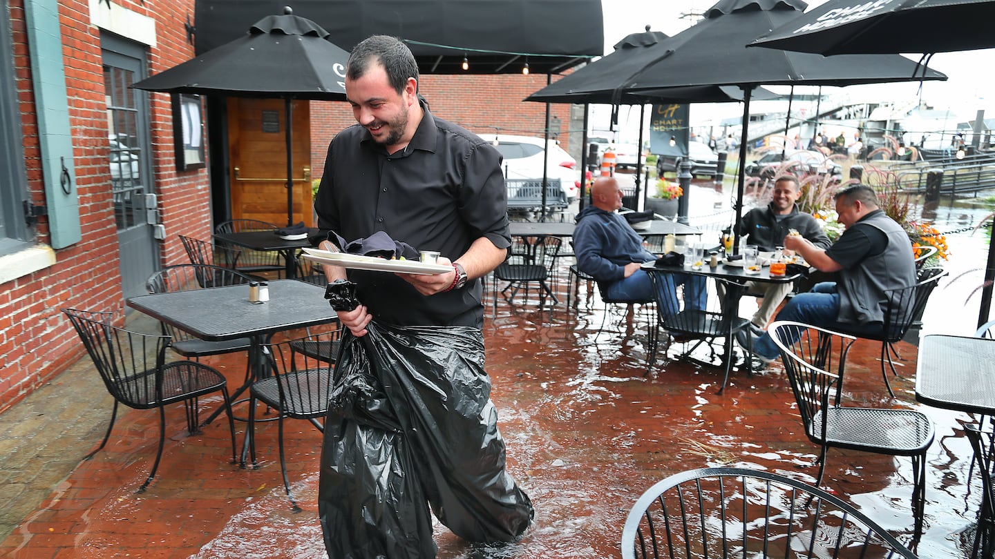 The high tide flooded sections of Long Wharf in Boston at its height just after 1 p.m. Joe Hebert, Greg Prall, and Rick Paoni had lunch on the outside patio of the Chart House on Long Wharf despite over a foot of water flooding the patio. Waiter Milan Grbovic used trash bags to keep dry while working.