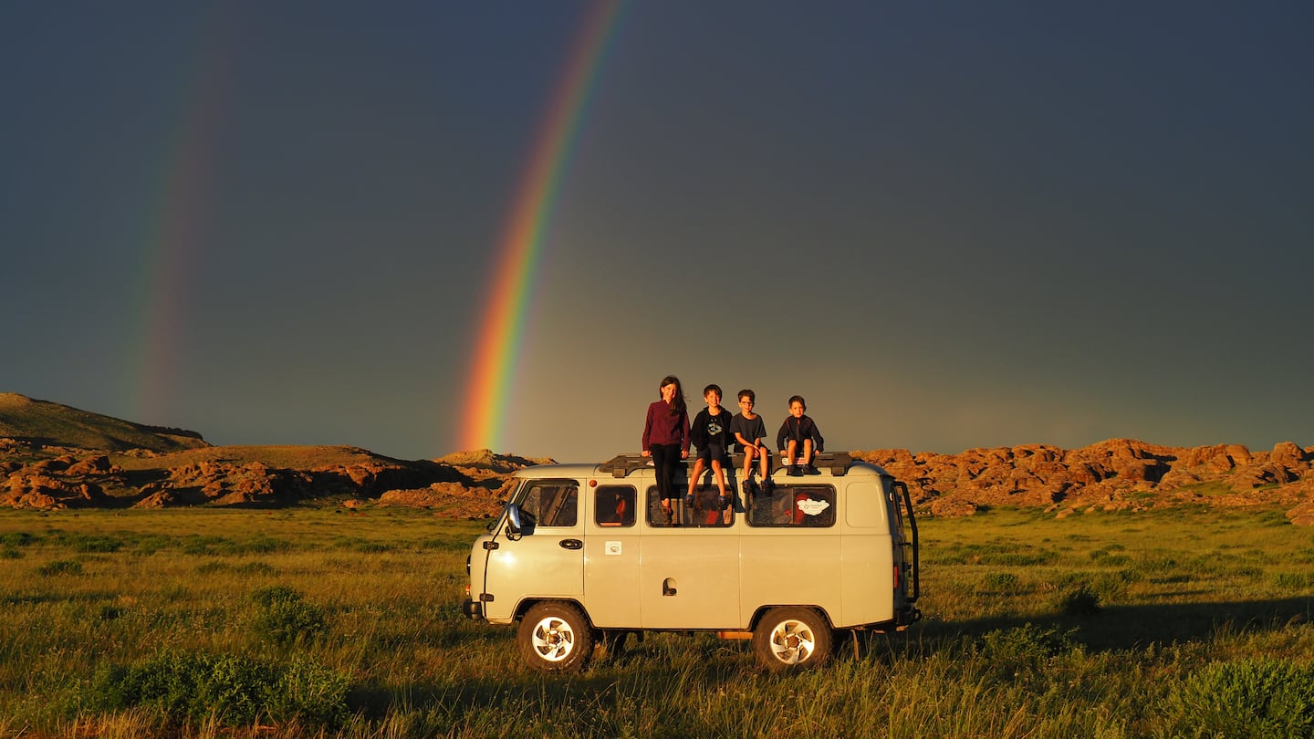 Mia, Léo, Colin, and Laurent Pelletier pose on top of their camper van in front of a double rainbow while in Mongolia.