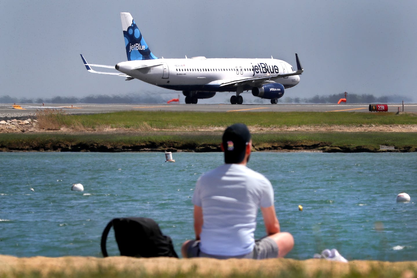 A man sat on Constitution Beach as a jet prepares for takeoff at Logan Airport across the harbor in May 2021.