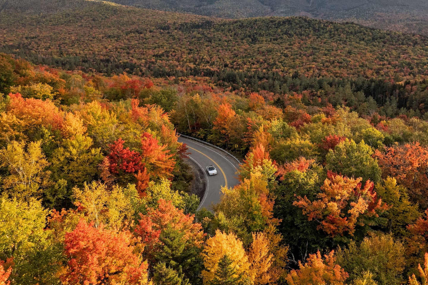 A car drives down the Kancamagus Highway in peak fall foliage.