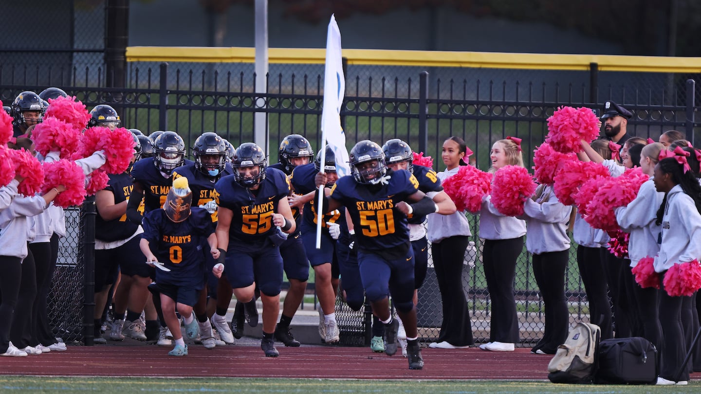 Adrian Lule (50) was the flag bearer as he leads the St. Mary's football team onto the field for Friday's Catholic Central matchup vs. Cathedral at the Manning Bowl. On the field, Lule registered a sack for a safety.