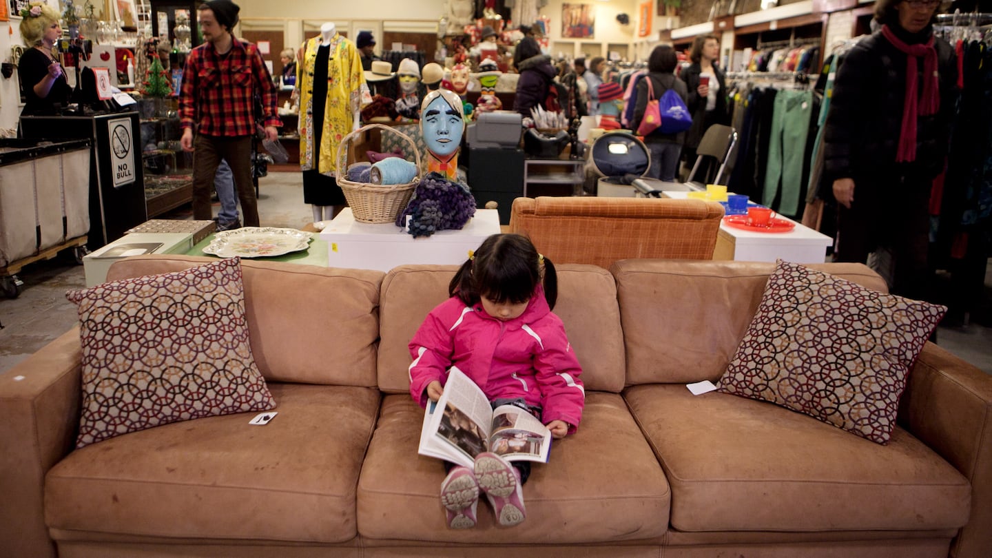 A child read a book while her mother shopped at the Boomerangs thrift store in Cambridge in 2013.