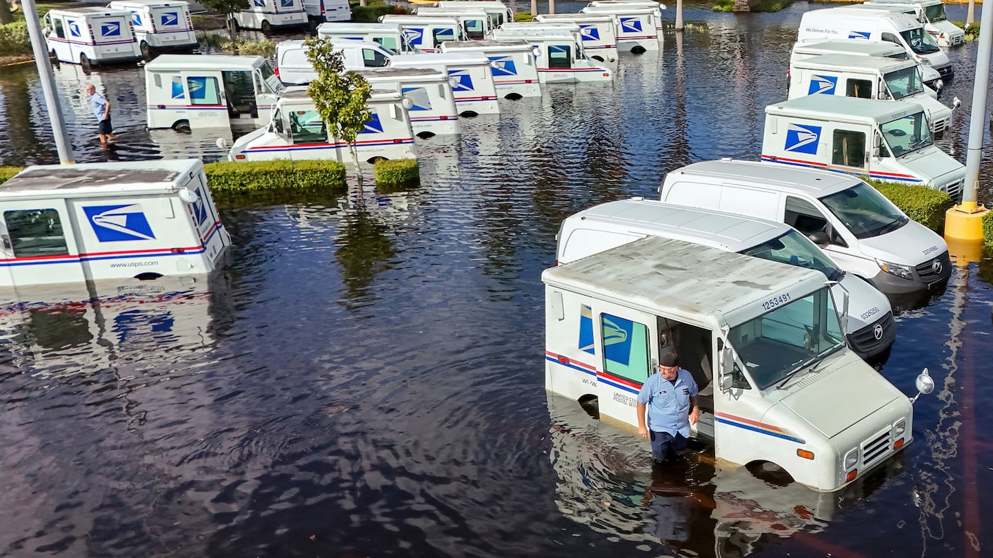 A USPS worker inspects trucks that had been relocated to protect them from wind but which are now underwater as intense rain from Hurricane Milton caused the Anclote River to flood, Friday, Oct. 11, 2024, in New Port Richey, Fla.