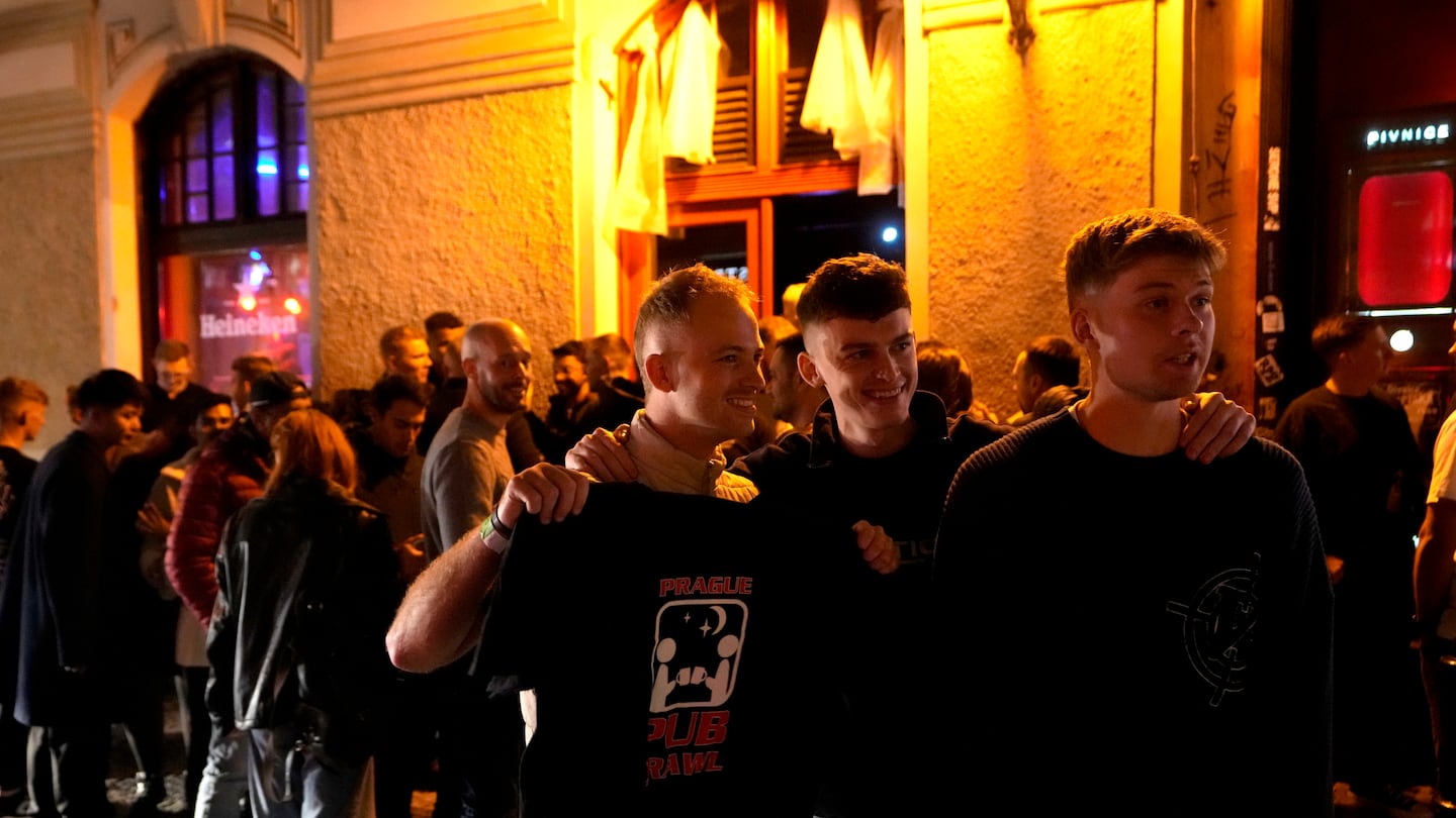 A group of tourists stand in line outside a bar as they attend a pub crawl tour in downtown Prague, Czech Republic, Thursday, Oct. 17, 2024.